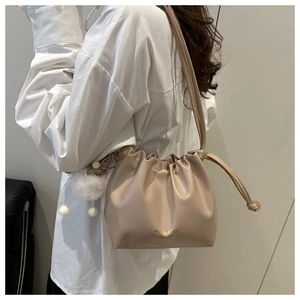 Detail of beige drawstring bucket bag with plush charm and golden fashion lettering