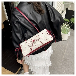 Détail d'un sac à bandoulière en toile crème avec nœuds rouges et breloque cœur