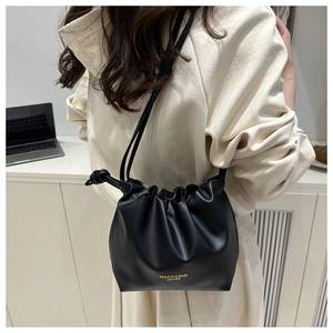 Model wearing a black drawstring bucket bag with gold fashion lettering and pleated detail