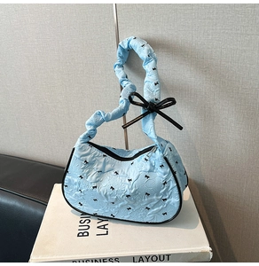 Close-up of light blue pleated hobo bag with black bow patterns and ruffled handle