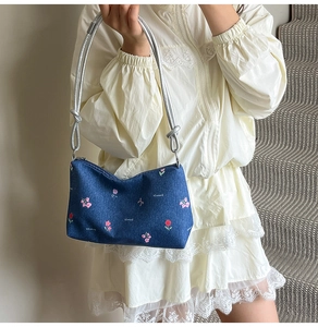 Detail of floral embroidery and silver rope strap on a denim shoulder bag worn by model