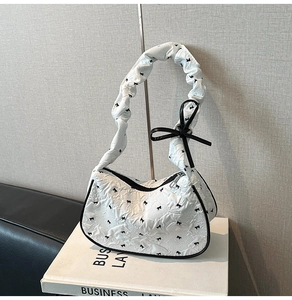 Close-up of white jacquard shoulder bag with black bow patterns and ruffled handle detail