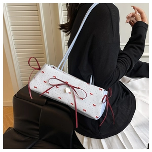 Détail du sac blanc avec nœuds rouges et pendentif cœur argenté sur un modèle