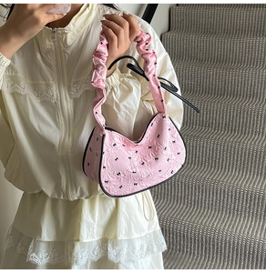 Detail of pink quilted shoulder bag with black bow patterns and ruffled handle texture