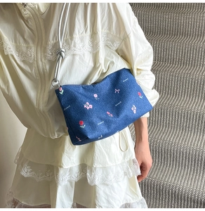 Close-up of floral denim underarm bag with pink flowers and silver chain on a model