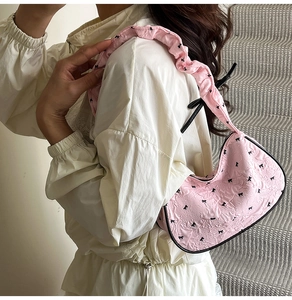 Detailed texture of pink pleated fabric bag featuring black bow prints and ruffled strap