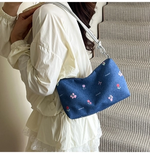 Detail of blue denim shoulder bag with floral embroidery worn by a model on stairs