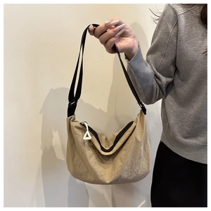 Detail of a khaki nylon shoulder bag with wide black strap and white triangular charm