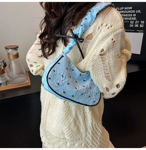 Close-up of light blue pleated shoulder bag with black bow embroidery and ribbon detail
