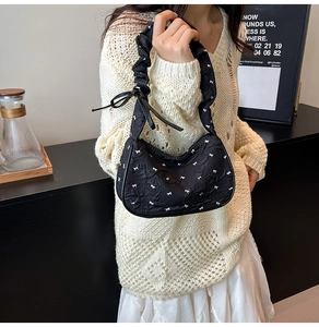 Detail of a black ruffled shoulder bag with white bow patterns on textured fabric