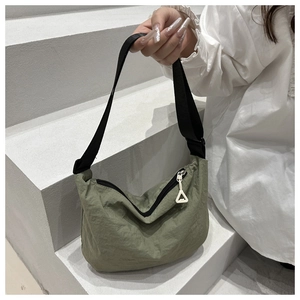 Close-up of sage green nylon shoulder bag with adjustable strap on white steps