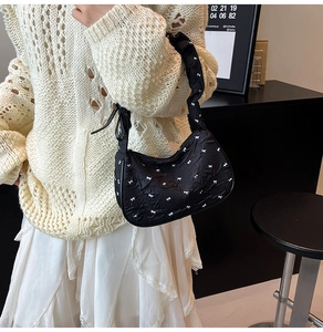 Detailed close-up of black pleated fabric underarm bag with white bow print patterns