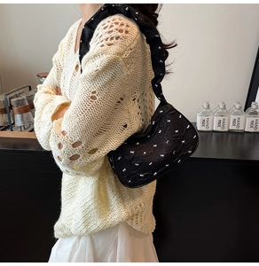 Detail of a black pleated shoulder bag with white bow embroidery on a textured fabric