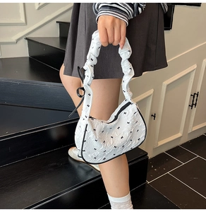 Detail of white pleated underarm bag with black bow patterns and ribbon handle