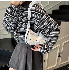 Detail of white half-moon bag featuring black bow patterns and pleated shoulder strap