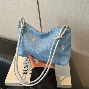 Blue denim handbag with floral print and silver rope handle held against business book
