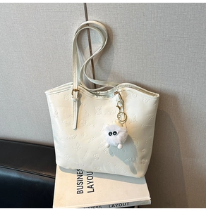 Detail of cream tote bag with floral 3D embossing and fuzzy ball charm on prop books