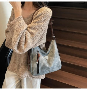 Model wearing large retro grey hobo bag with brown leather straps on a wooden staircase