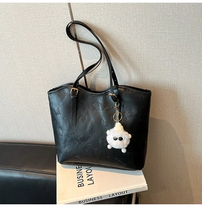 Detail of black tote bag featuring embossed dog and butterfly motifs with plush lamb charm