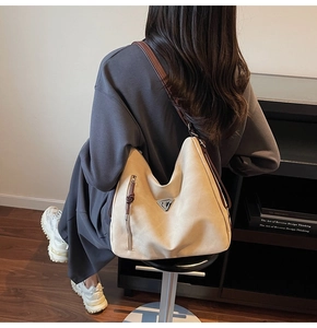 Detail of beige hobo shoulder bag featuring vertical zipper and metallic triangle accent