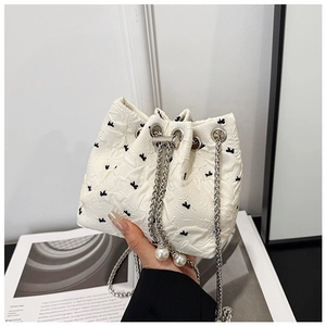 Detail of white quilted bucket bag with black bow embroidery and pearl drawstring charms