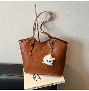 Detailed texture of brown embossed tote bag with floral puppy patterns and plush charm