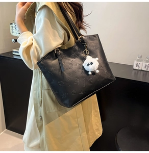 Detail of vintage black tote bag featuring embossed patterns and a white plush charm