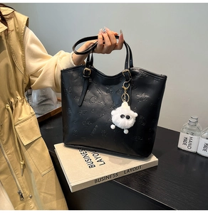 Detail of black leather tote bag with embossed fashion patterns and plush sheep pendant