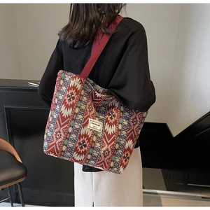 Rear view of a model wearing a large red bohemian woven tote bag with geometric patterns