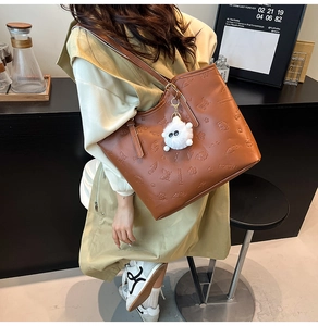 Detail of a brown tote bag featuring embossed textures and a white plush ball accessory