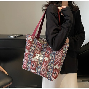 Ethnic style woven tote bag with geometric patterns and red wide strap shown on a model