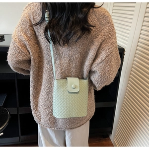Detailed view of mint green woven mini bucket bag worn by model in a modern home setting
