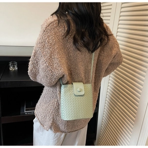 Detail of mint green woven texture bucket bag with crossbody strap on woman model