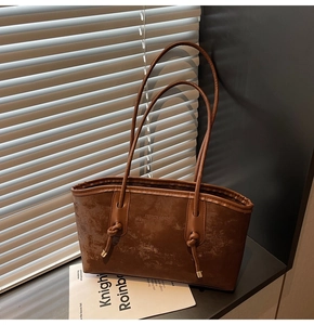 Detailed macro of vintage brown matte leather tote with embossed fashion logo and knot strap