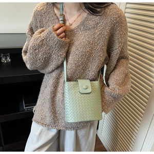 Detail of light green woven bucket bag with magnetic flap worn by a model in a cozy home