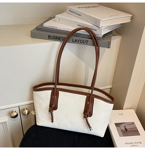 Detail of a cream tote bag featuring brown trim and knotted handle with embossed logo
