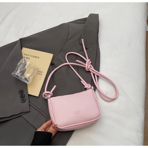 Pink lychee texture mini crossbody bag with knot shoulder strap on a grey blazer and book