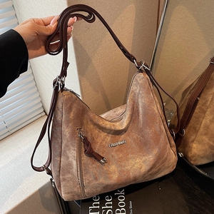 Brown vintage suede tote bag with adjustable strap and metal fashion logo on a mirror