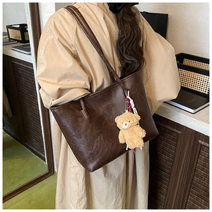 Detail of dark brown leather tote bag with FASHION lettering and plush bear accessory