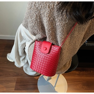 Detail view of red woven leather bucket bag with flap cover worn by a model in a cozy room
