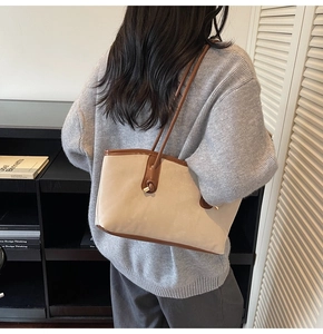 Detail view of large beige tote bag with brown leather handles and gold metal accents