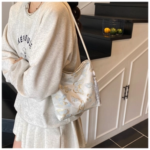 Close-up of white satin bucket bag with butterfly embroidery and silver fringe tassels