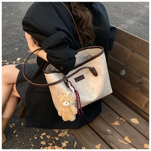 Detail of vintage tote bag with plush bear charm and woven rope on model in autumn setting