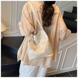 Close-up of golden jacquard landscape embroidery and tassel detail on the shoulder bag