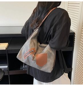 Detailed view of a grey canvas tote bag with brown leather pockets shown on a model