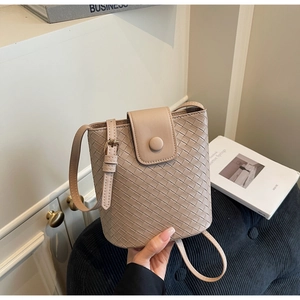 Close-up of beige woven leather bucket bag with top flap and adjustable strap