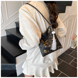 Detail of black shoulder bag featuring golden butterfly embroidery and jade tassel pendant