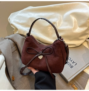 Detail van vintage bordeauxrode suède tas met leren strik en zilveren hartvormige hanger