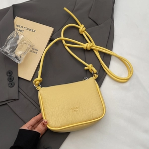 Mini yellow crossbody bag with litchi texture and stylish knot strap on grey blazer background