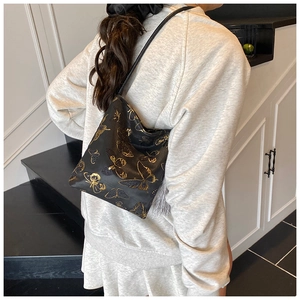 Close-up of black shoulder bag featuring gold butterfly prints and grey silk tassels